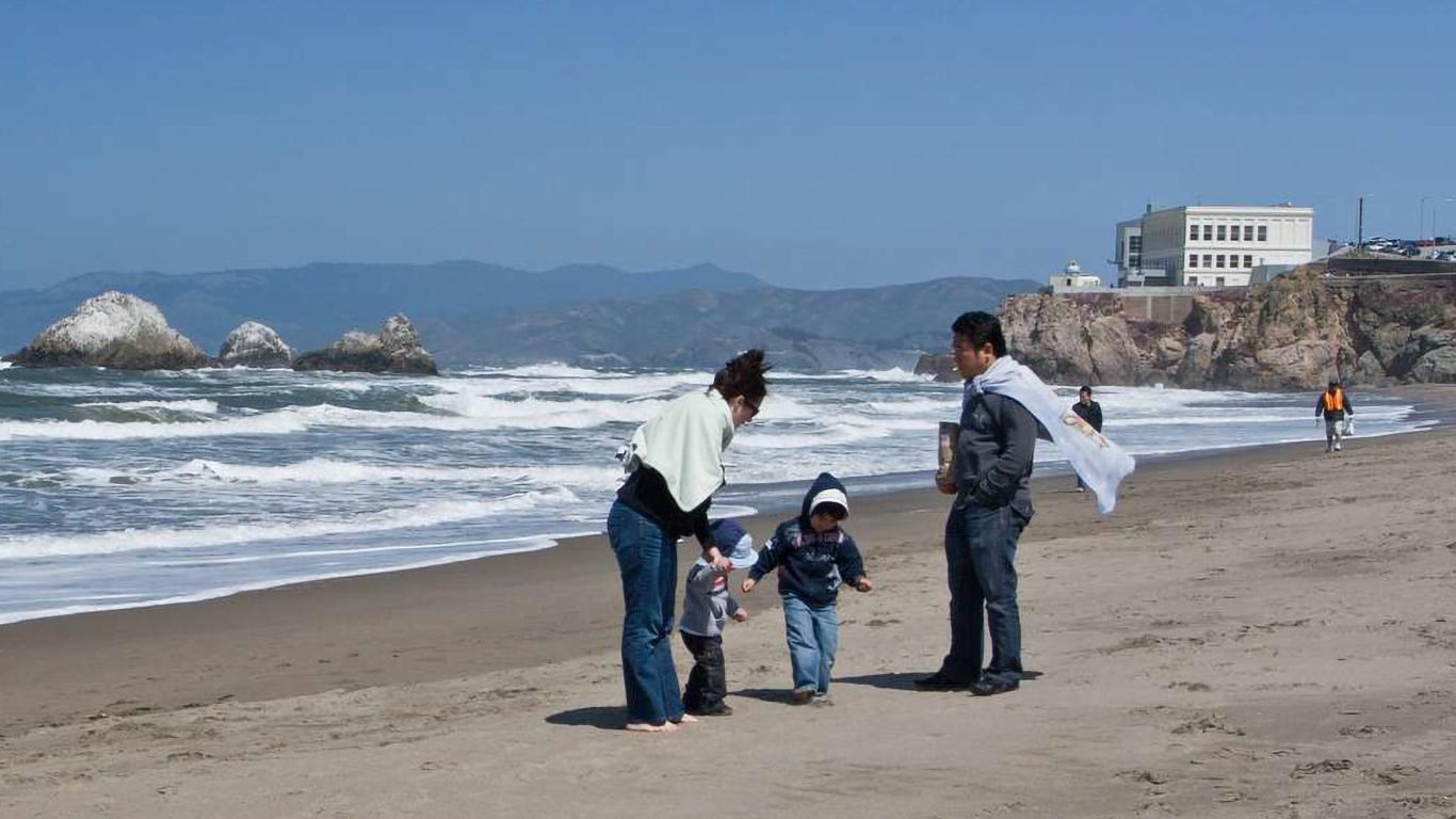 A family enjoys Ocean Beach, The Cliff House can be seen above them in the distance.