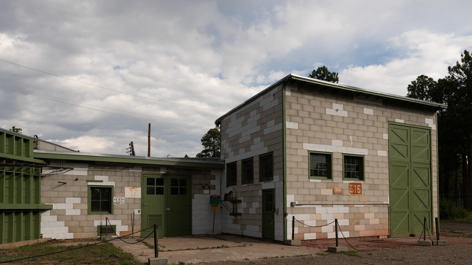 A large building made of gray stone blocks with green doors sits under a cloudy sky.