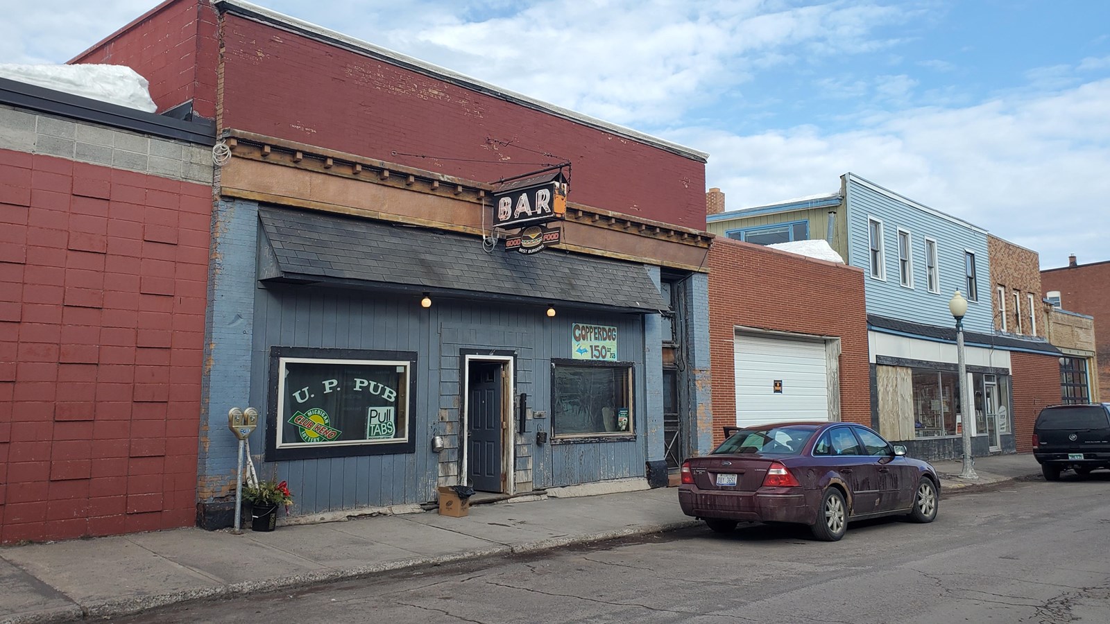 Two story brick, concrete block, and wood building with sign above the door reading βbar.β