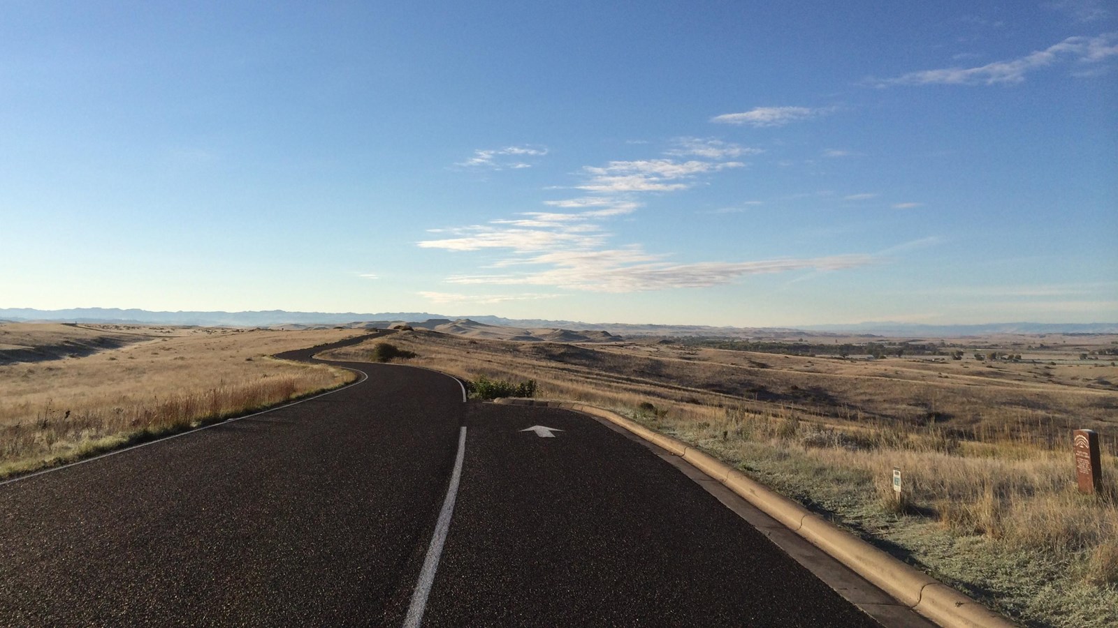 a black asphalt road stretches away into a blue sky with a pull off and wayside to the right