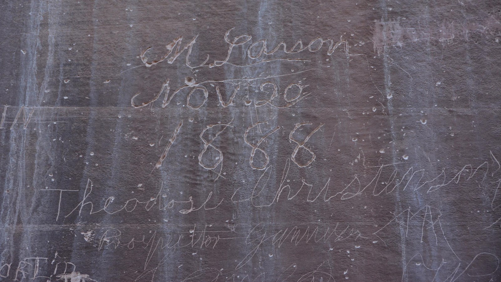 signatures carved into reddish rock wall. 