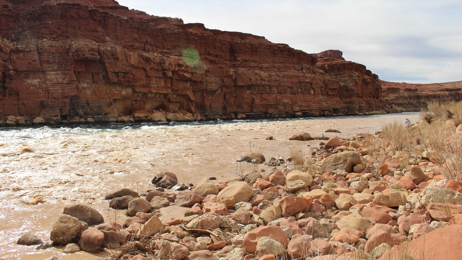 Muddy Paria River mixing into the blue Colorado River. Canyons rise from behind the Colorado River. 