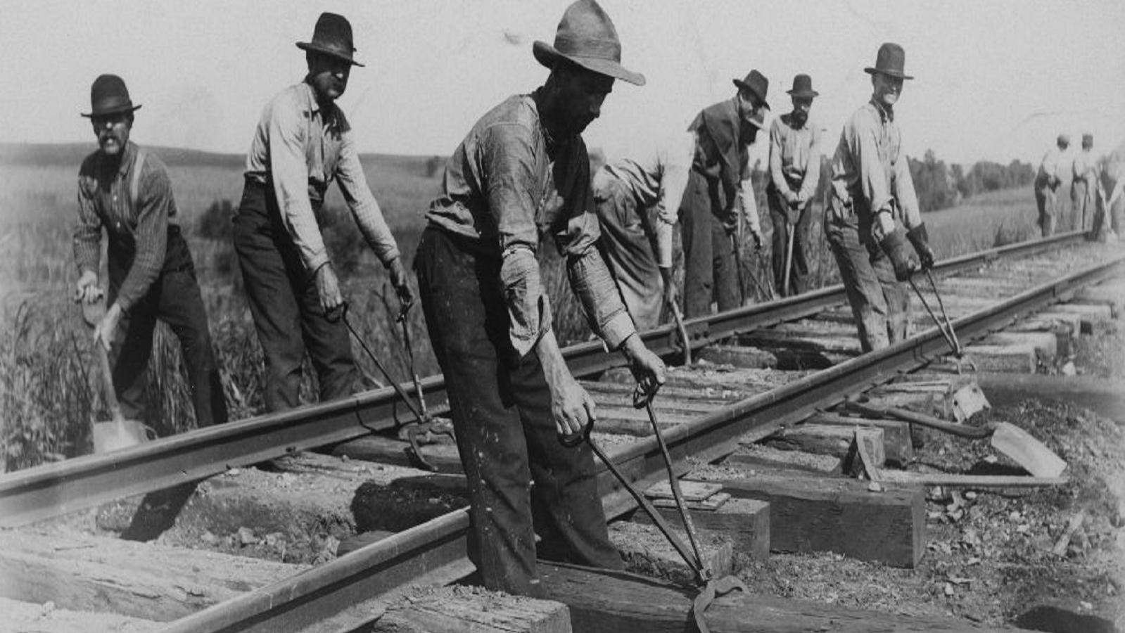 Black and white photo of men working on laying down railroad tracks in 1900.