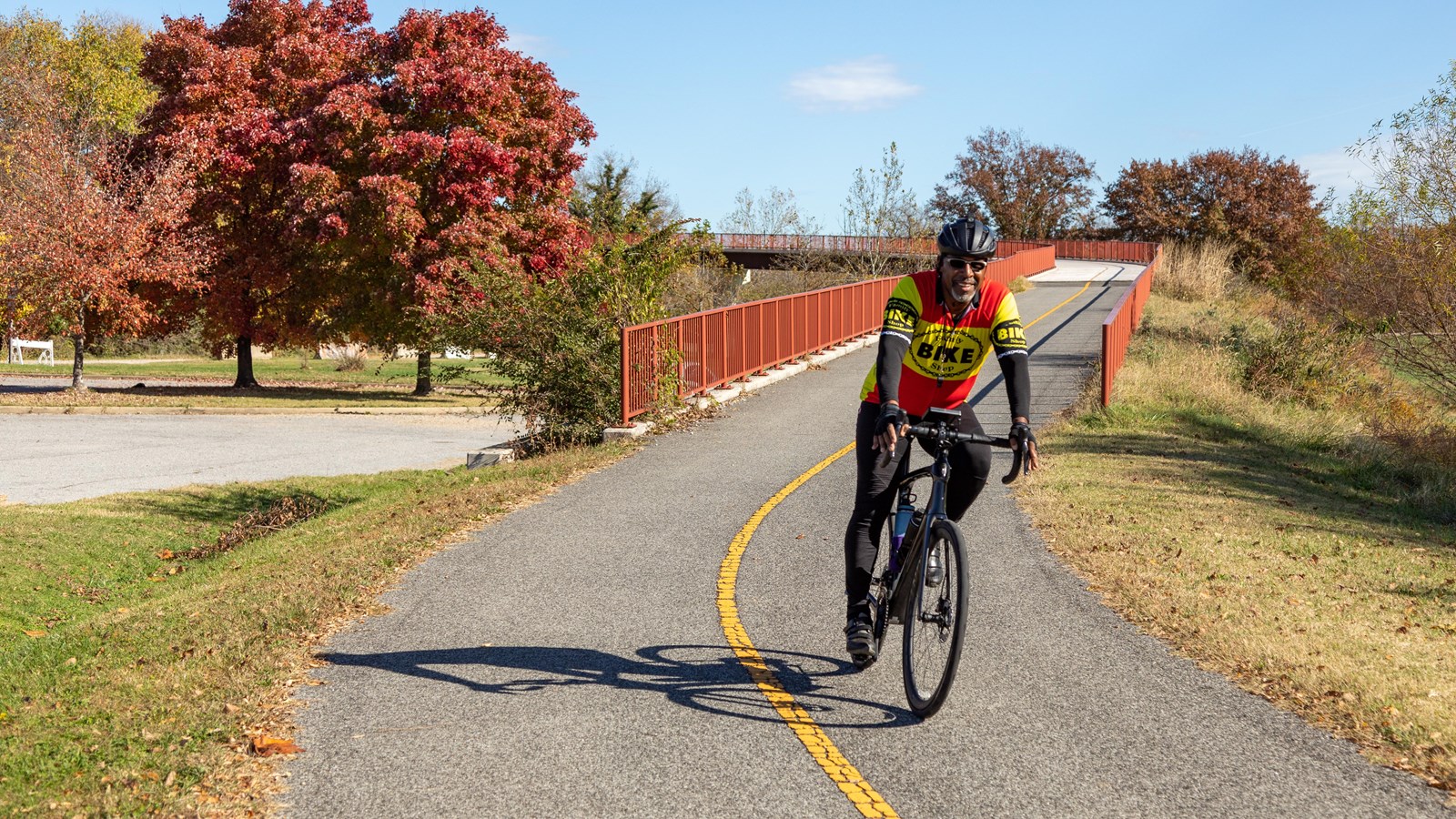 A man smiles as he rides his bicycle down a paved trail.