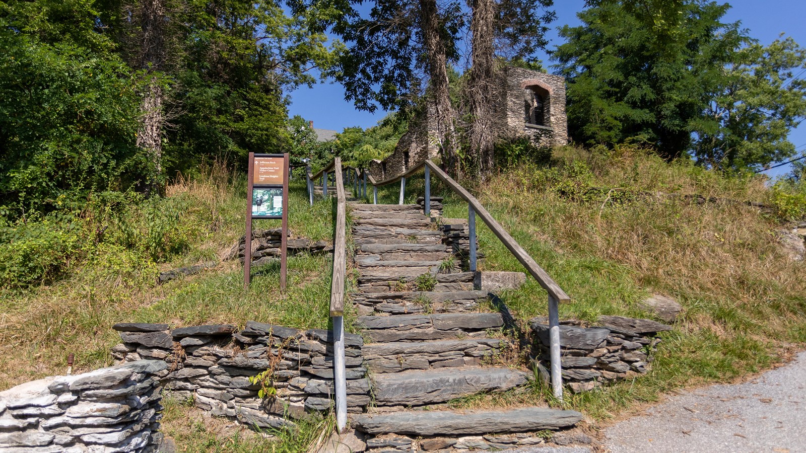 a 2 panel sign stand to the left of stone steps and a handrail
