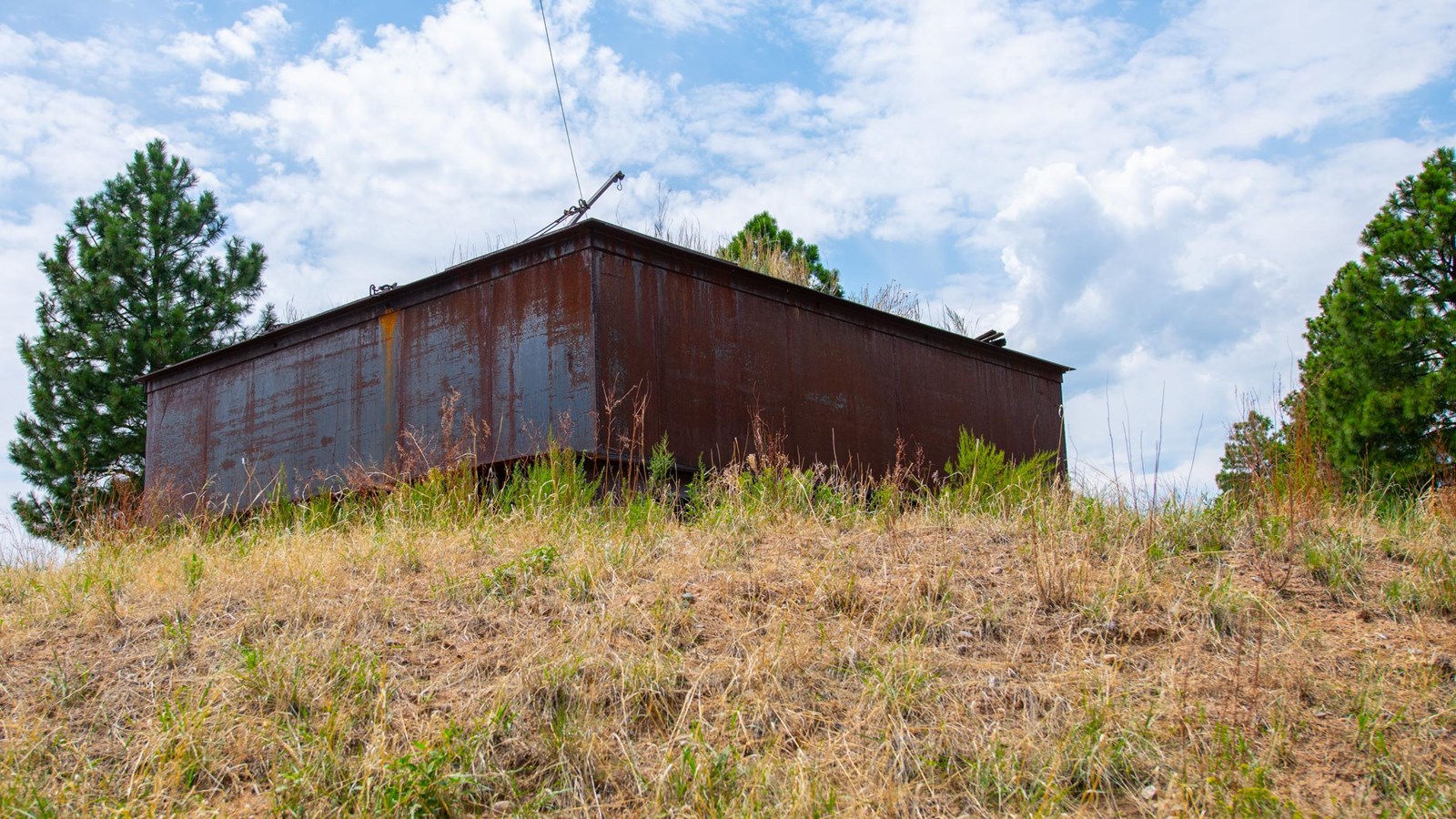 A rusty structure stands atop a rounded grassy hill.