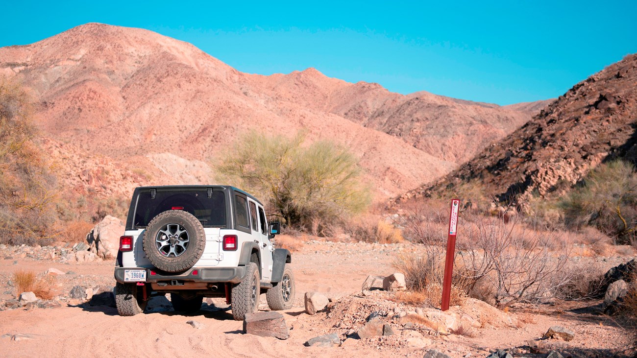 A Jeep turns from one dirt road to another next to a boundary marker.