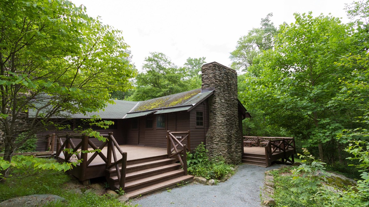 An historic cabin with a large porch sits in the middle of a forest.