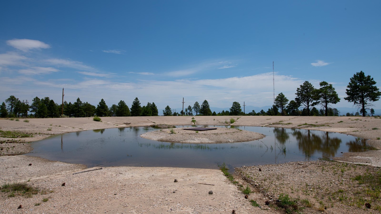 Standing water partially fills a large concrete depression in the ground.