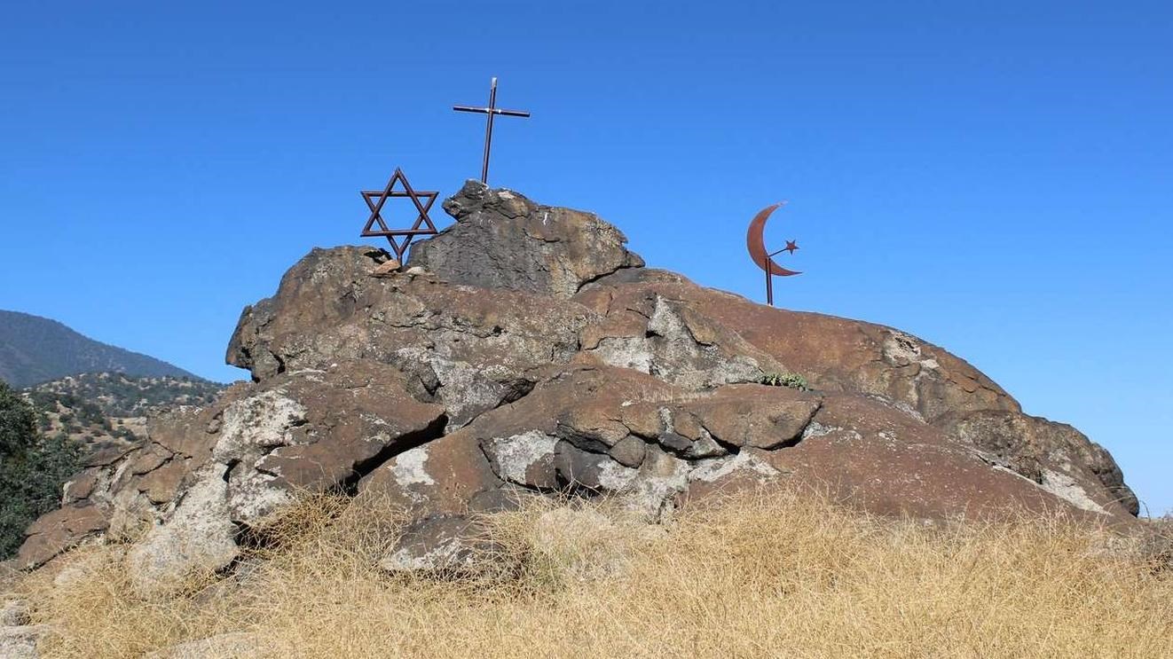 A rock formation with metal symbols of a cross, a star, and a moon, with dry grass in the foreground