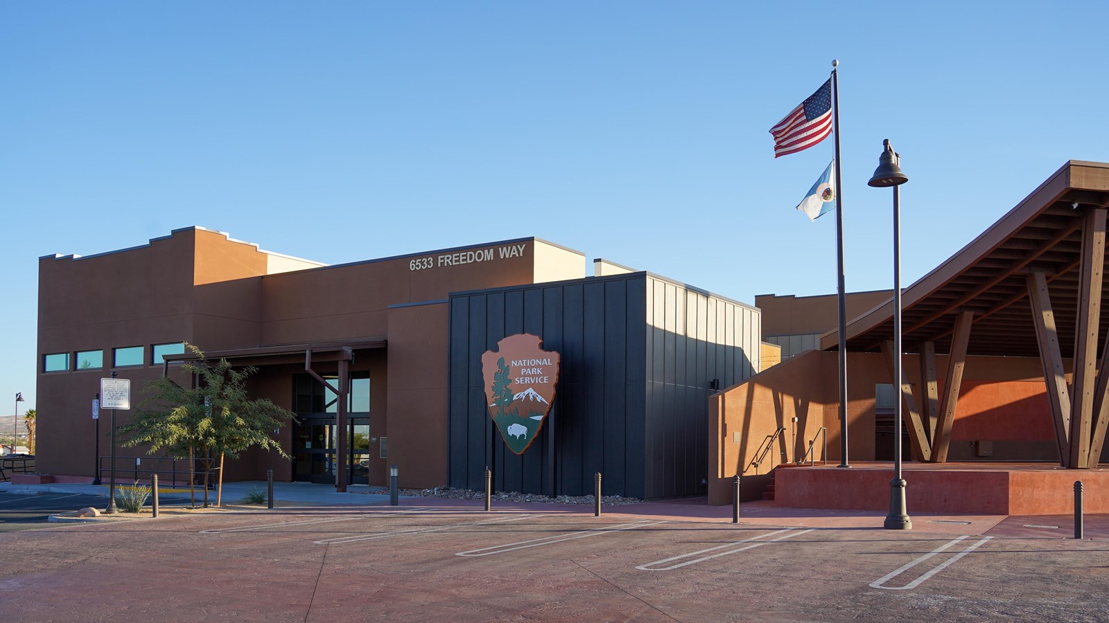 A large brown and black building with an NPS arrowhead. A flagpole stands next to the parking lot.