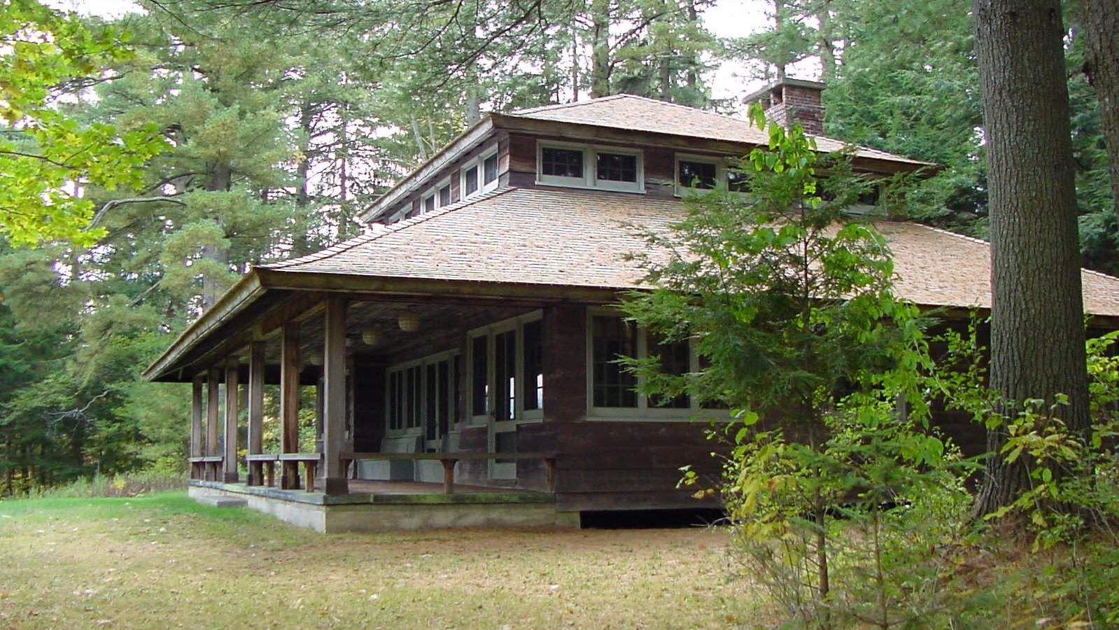 Wooden building with large covered porch surrounded by trees