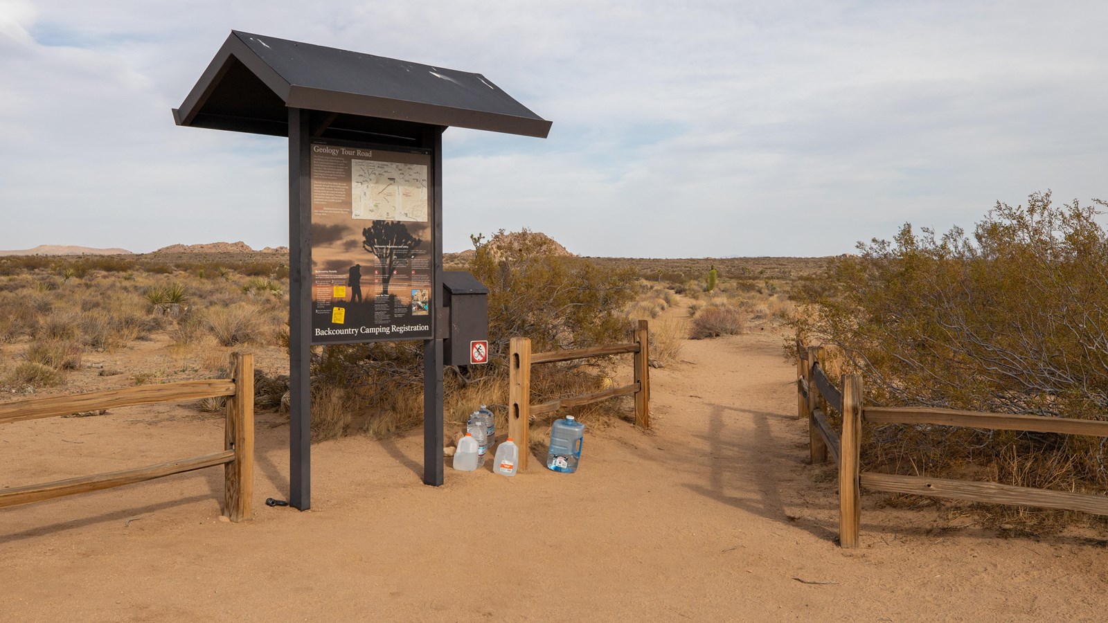 An information board next to a trailhead with a short wooden fence. 