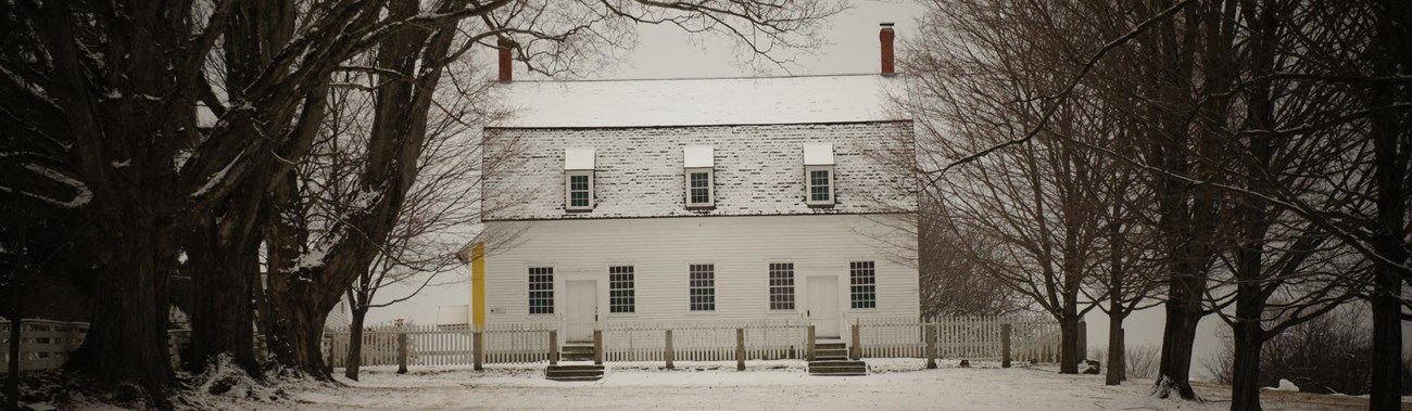 tree flanked common leading to a white clapboard building