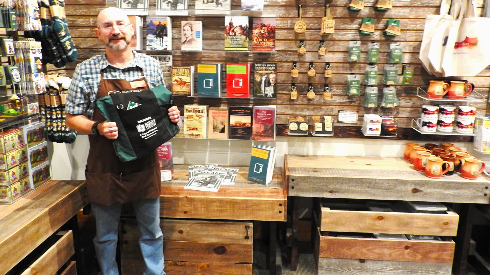 A man wearing a green apron stands in front of displayed merchandise. 