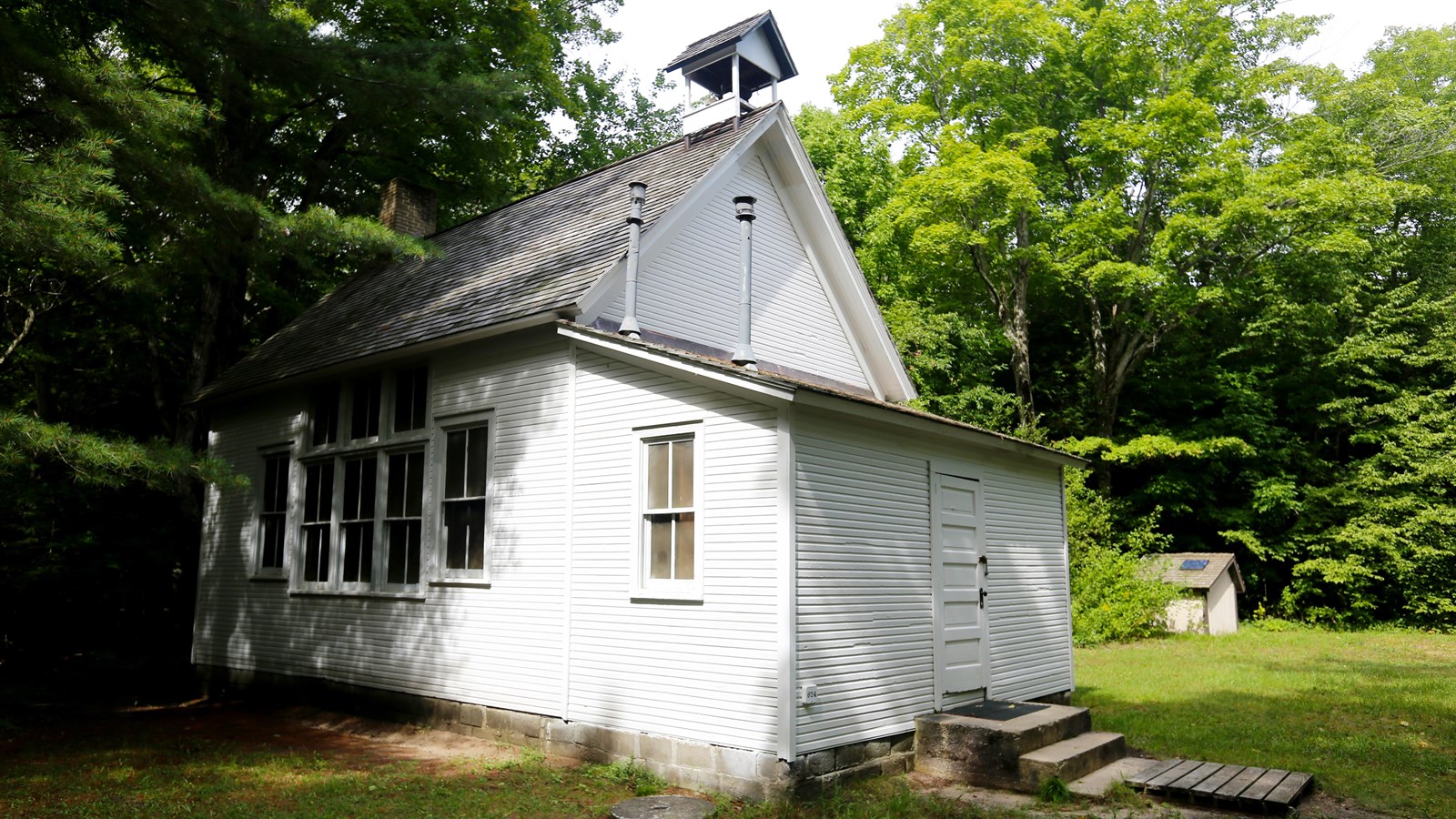 White clapboard building with a gabled roof with a bell at the peak