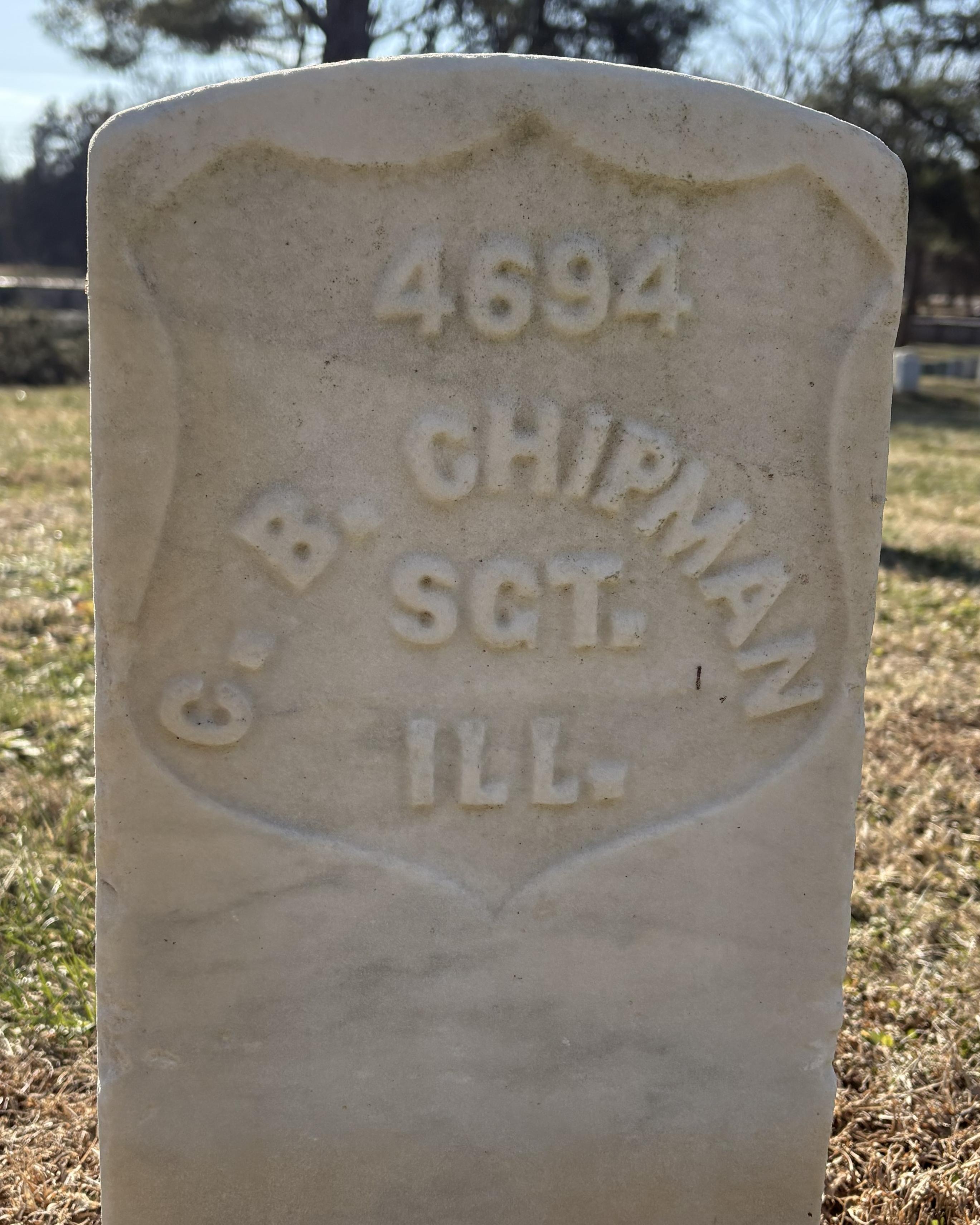 Marble headstone with grass and trees behind it. 