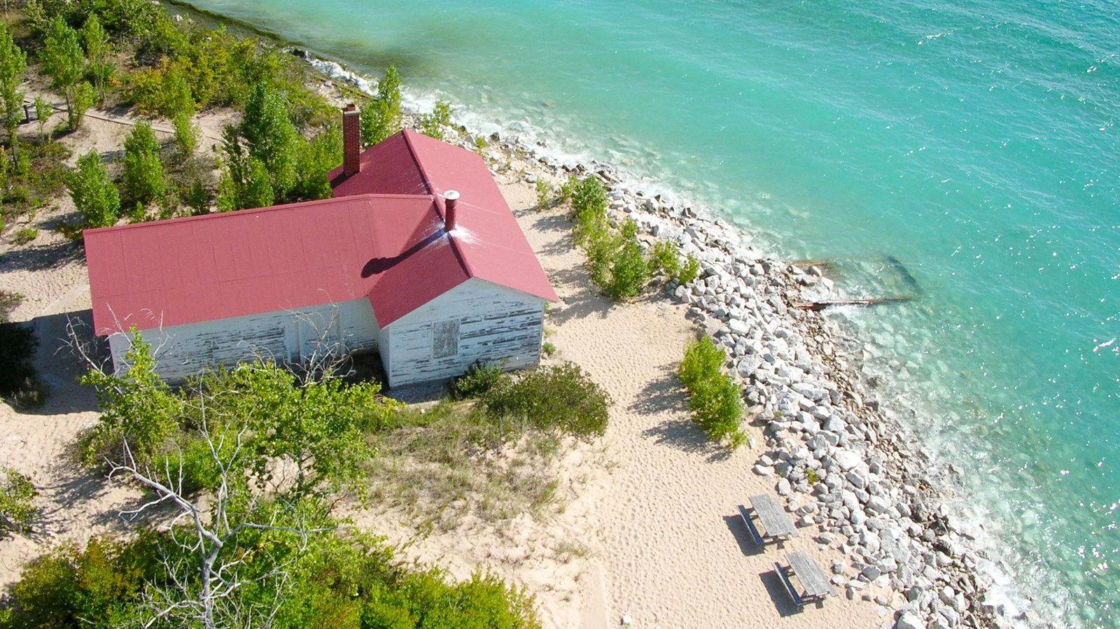 Looking down to red-roofed t-shaped building on beach alongside turquoise water