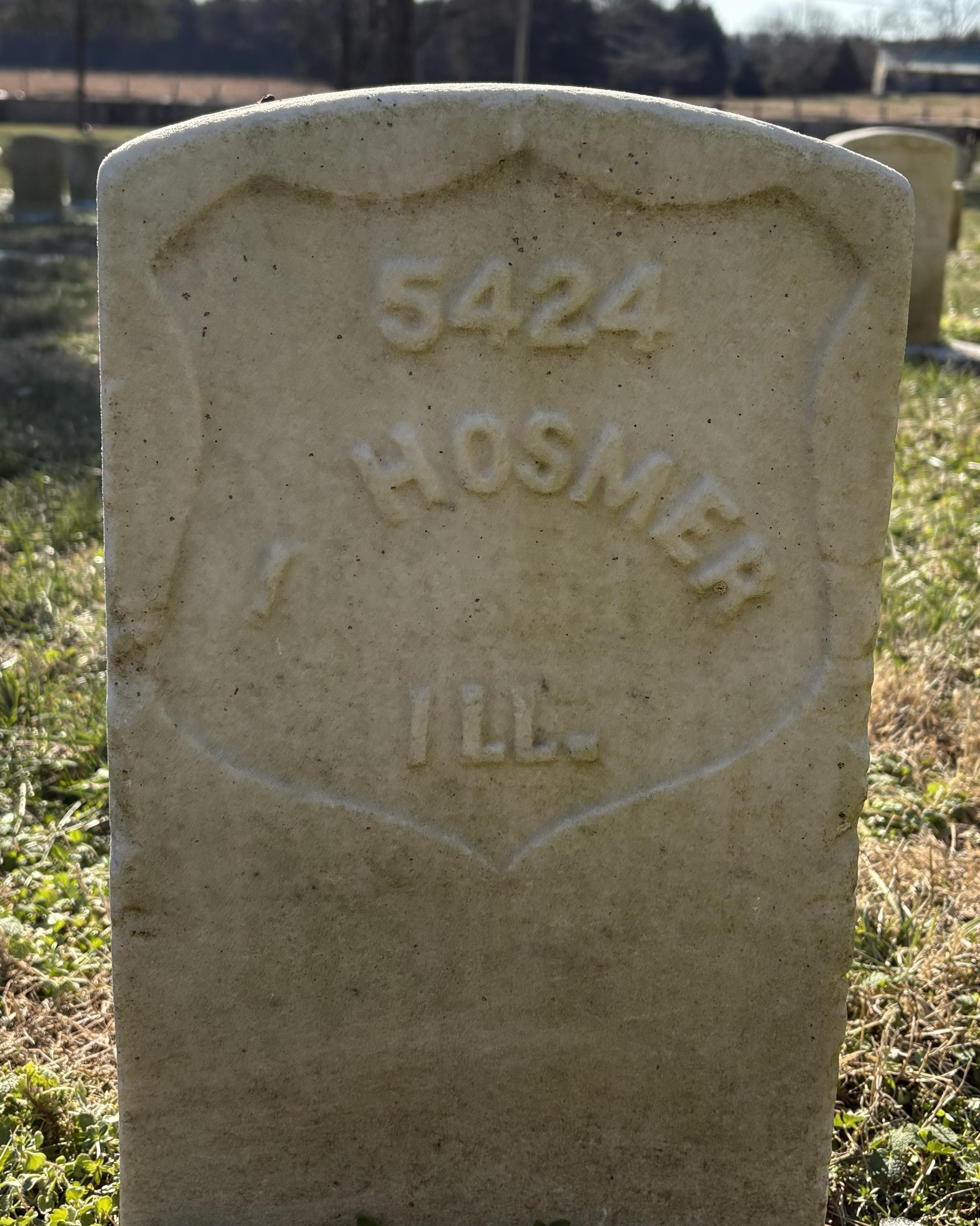 Marble headstone with grass behind it and snow in front of it.
