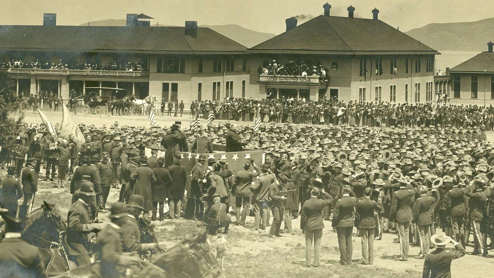 A sepia colored image of a crowd surrounding a President McKinley standing atop a raised platform.