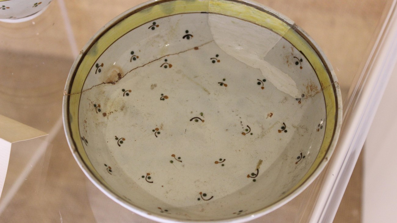 A white ceramic saucer with a small decorative design and yellow rim.