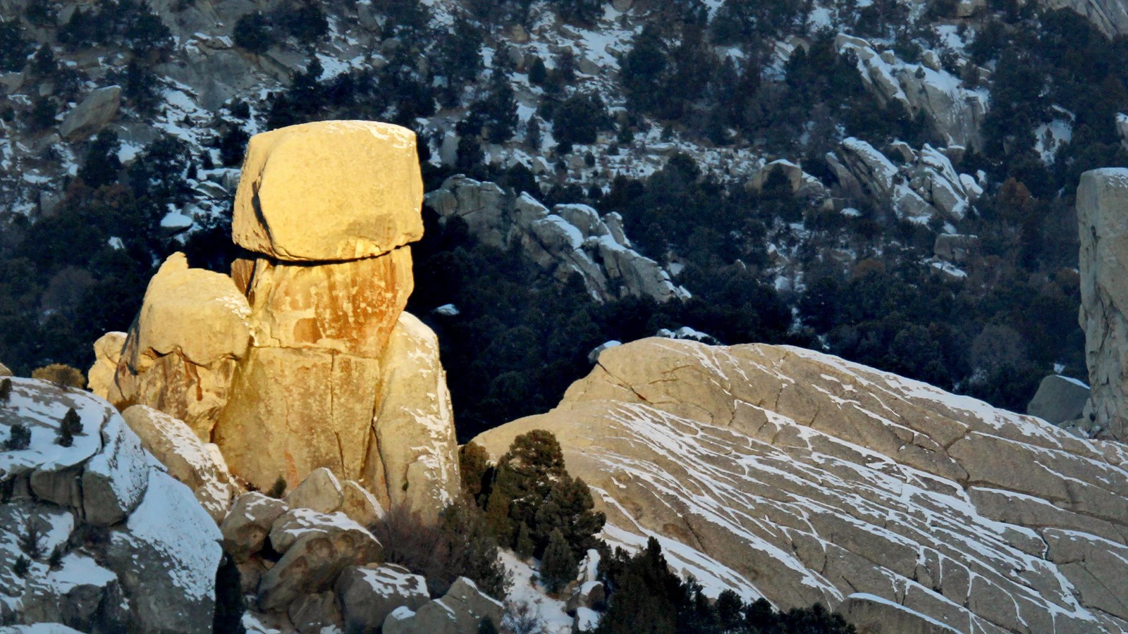 Box top rock glowing with sunlight with the rest of the landscape in snowy shadow.