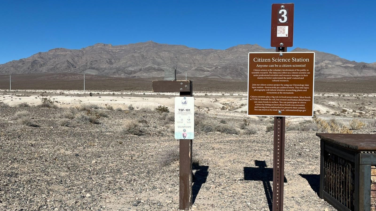 A brown wooden post with a gray block attached to the top next to a brown metal sign.
