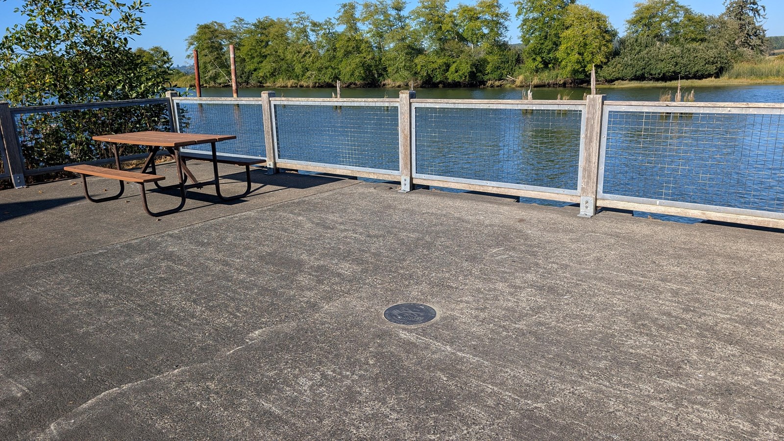 A small circular NGS marker is embedded into the concrete on a pier overlooking a river.