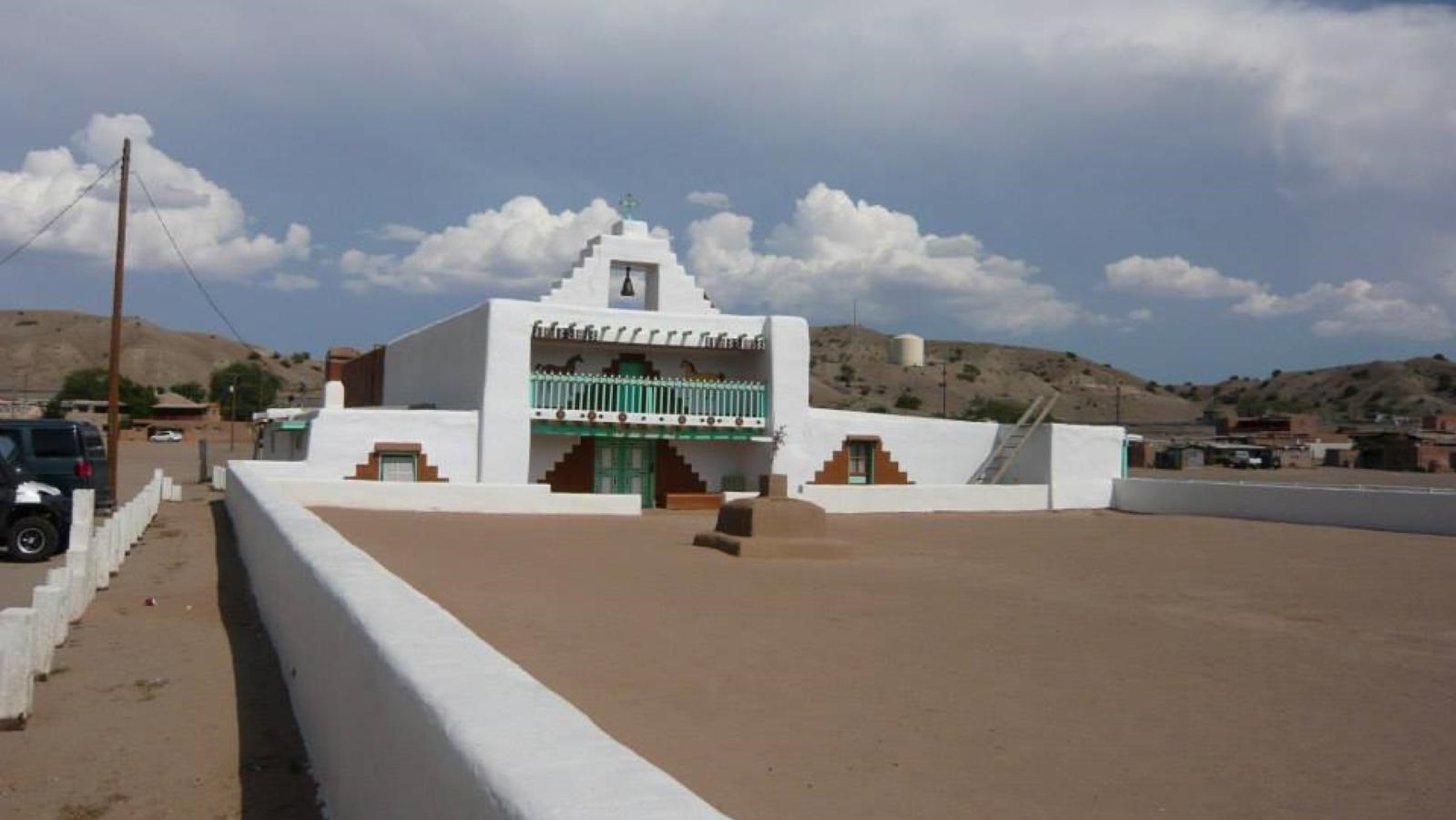 A white stucco building with teal detailing. Out front is a patio area surrounded by a short wall.