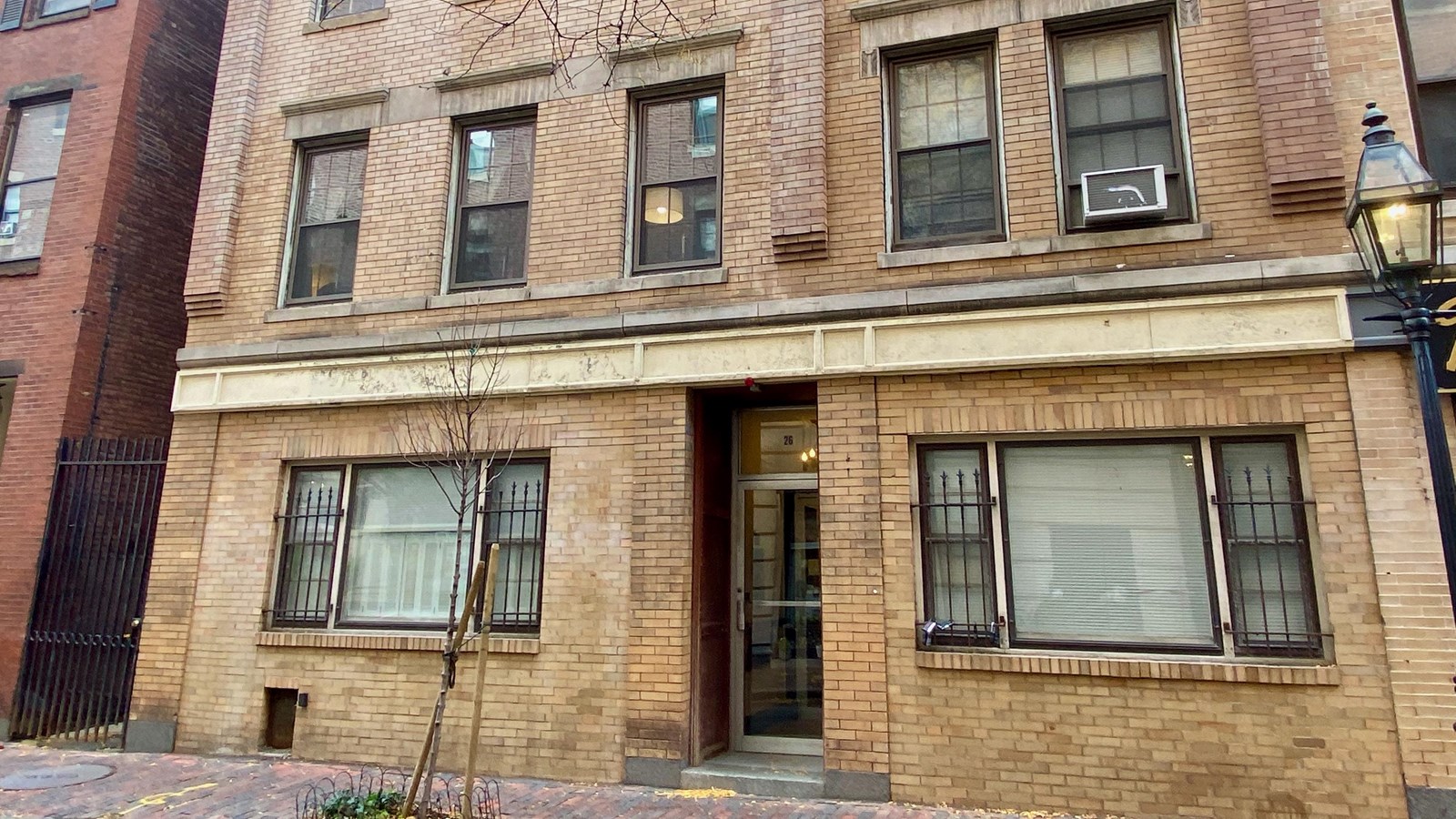 Multi-story light brick building with two large windows on either side of the front door.