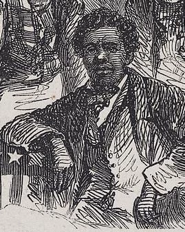 A man sits in a suit with one arm leaning on a table with and American flag.