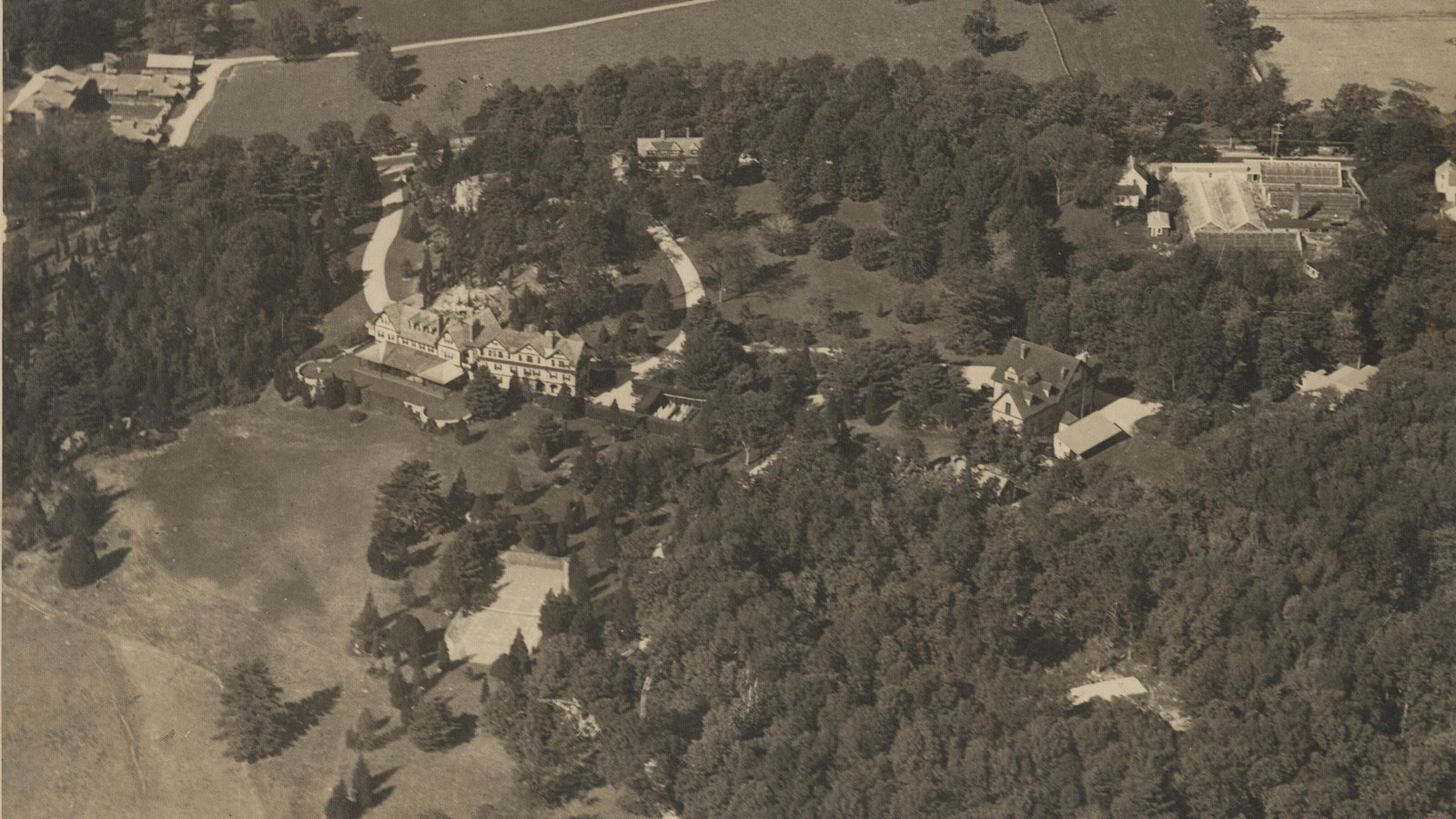 Black and white aerial of large estate with lots of trees and little open space in front