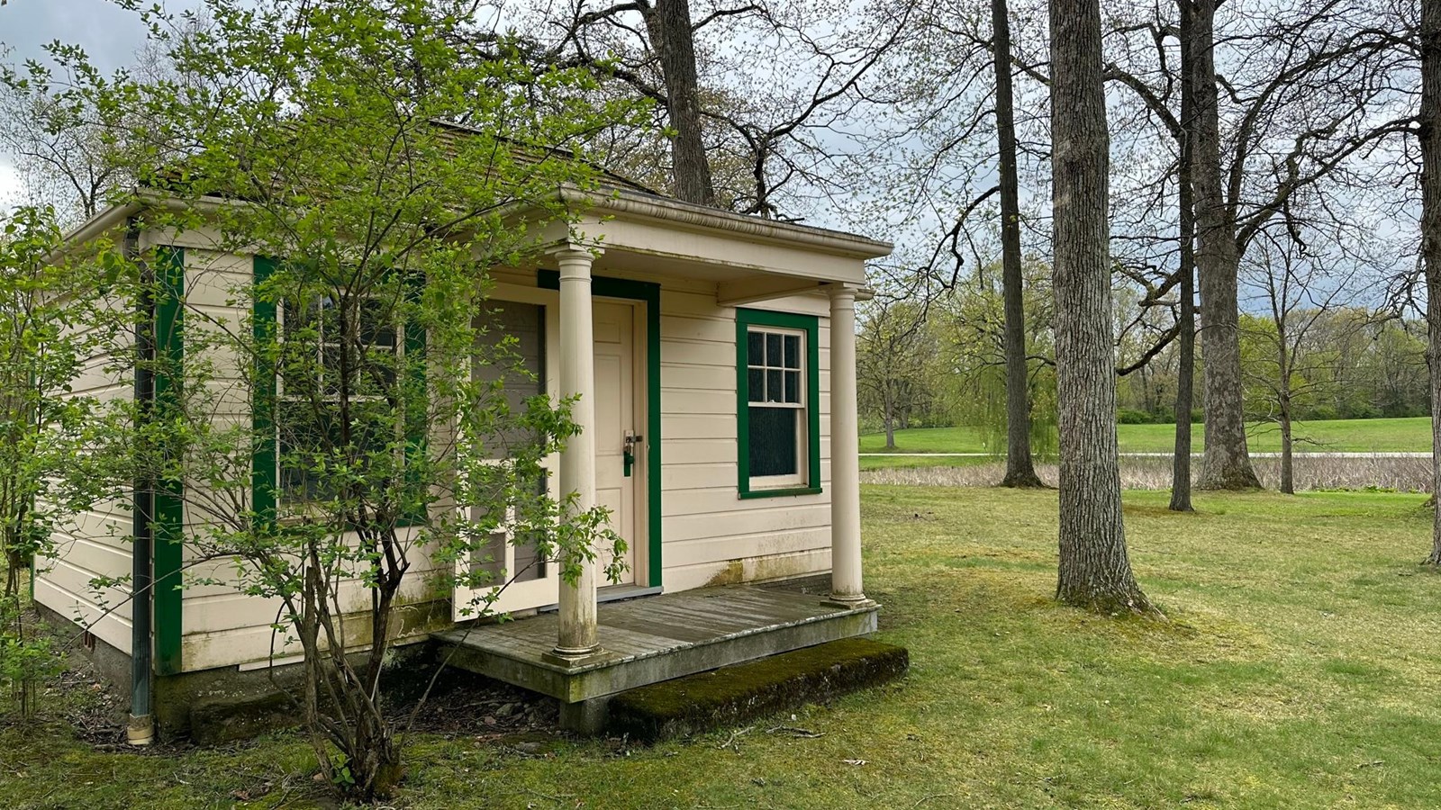 A small wood cottage with central porch situated next to a pond. 