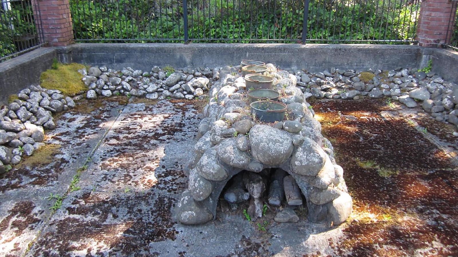 Five metal kettles sit on top of a rock half-cylinder structure, with a hollowed area underneath.