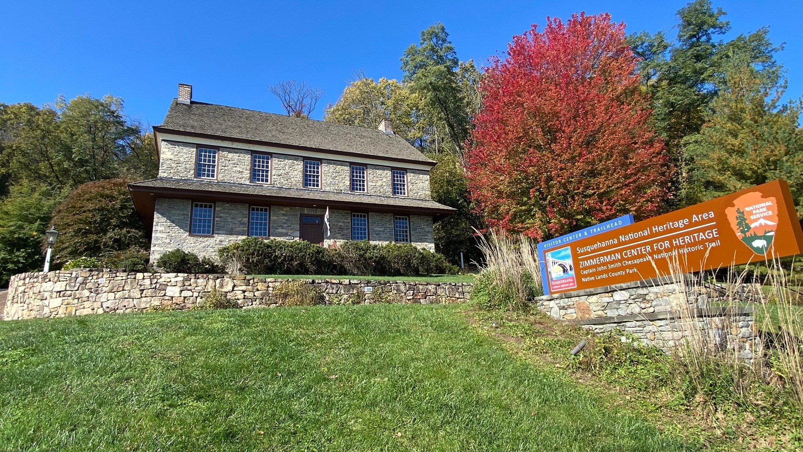 A historic stone building surrounded by trees and a sign in the foreground.