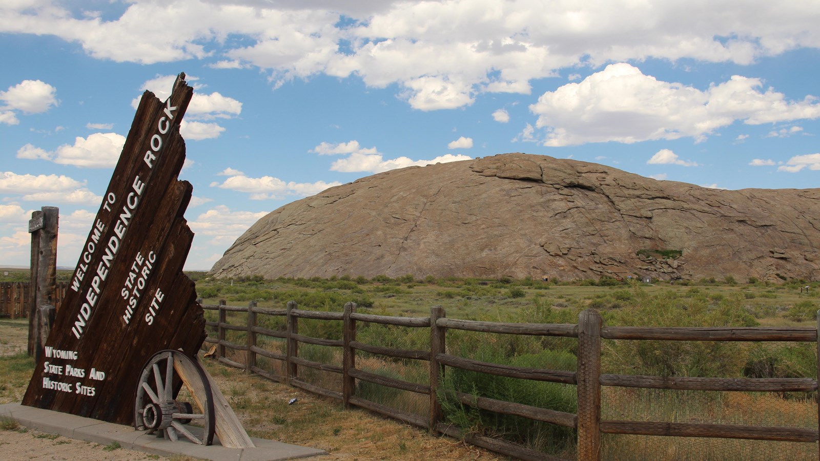 A sign sits in front of a smooth buttress set against a bright blue sky, and grassy valley.