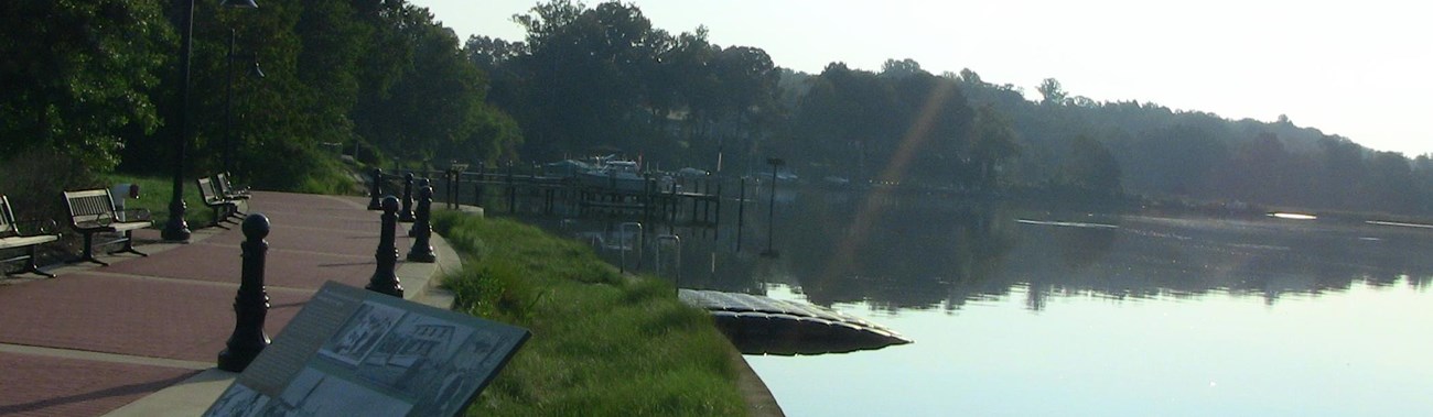 a curving concrete pathway and green border along water with a sloping kayak launch