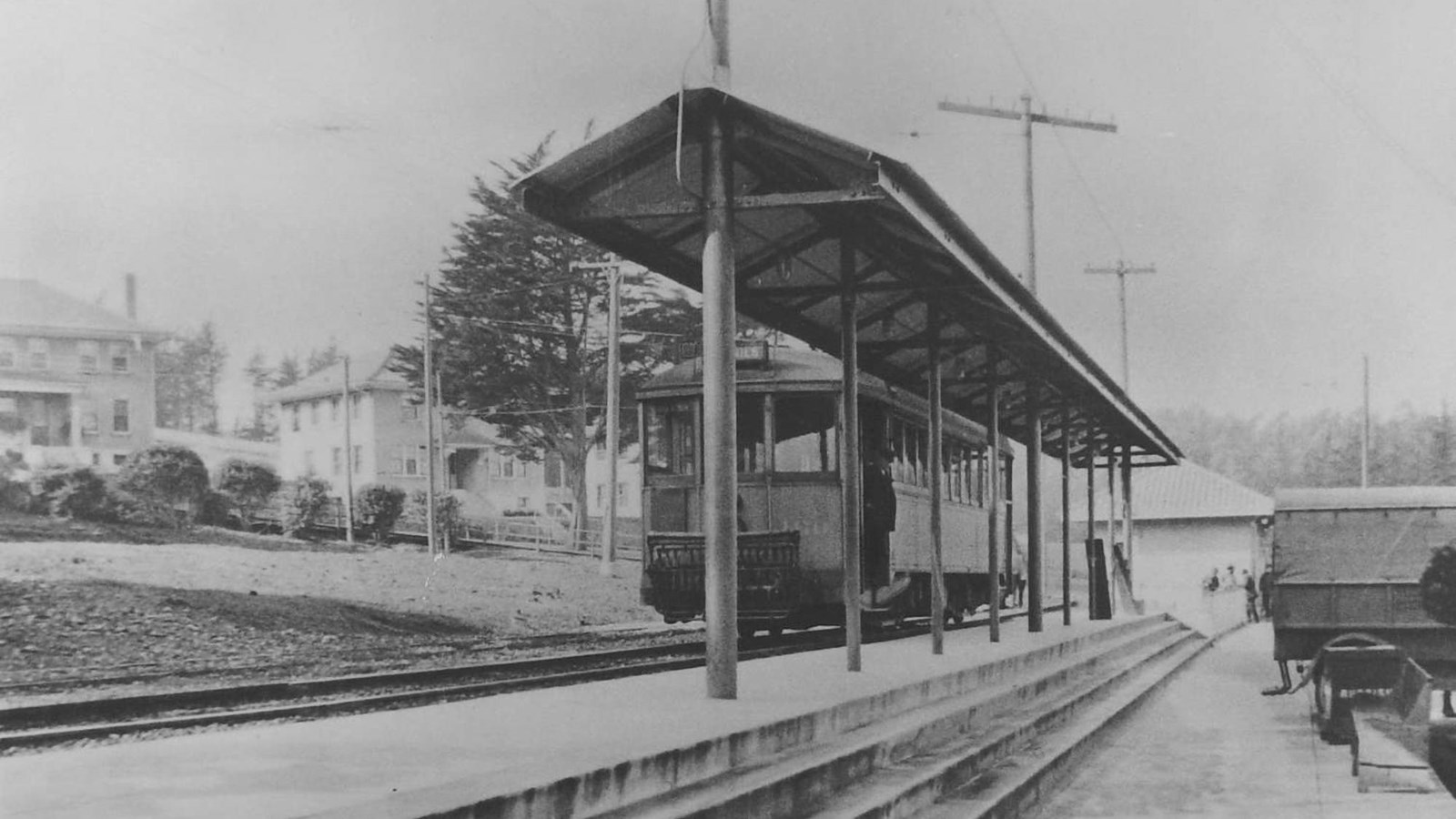Black and white image of a trolley car sits at a station.