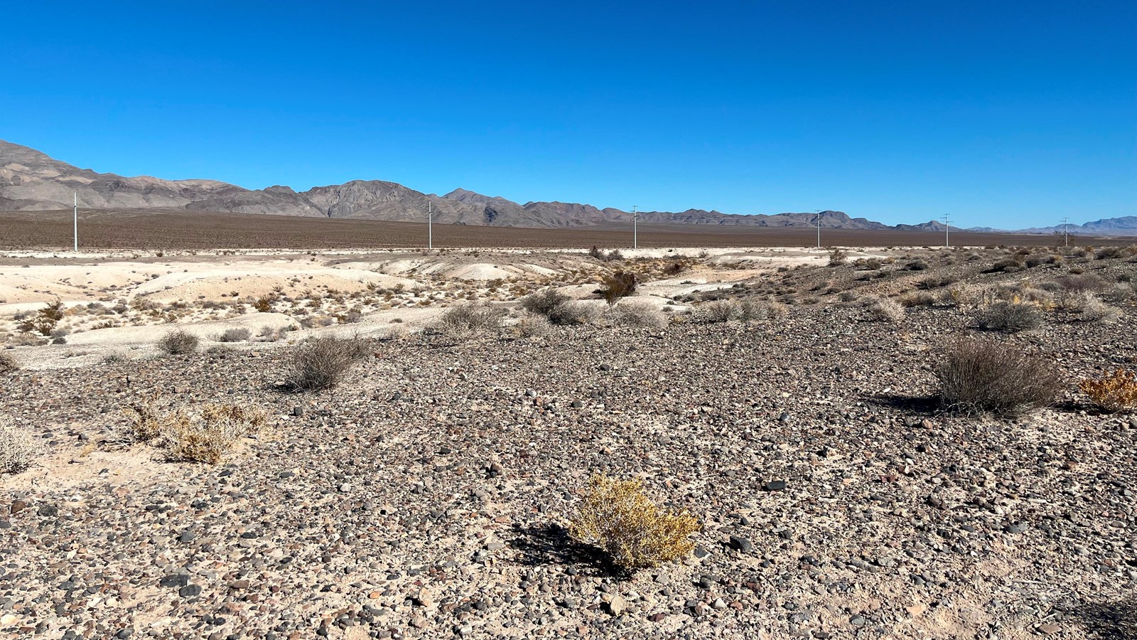 Gravel in the foreground slopes into tan hills with a mountain range in the background