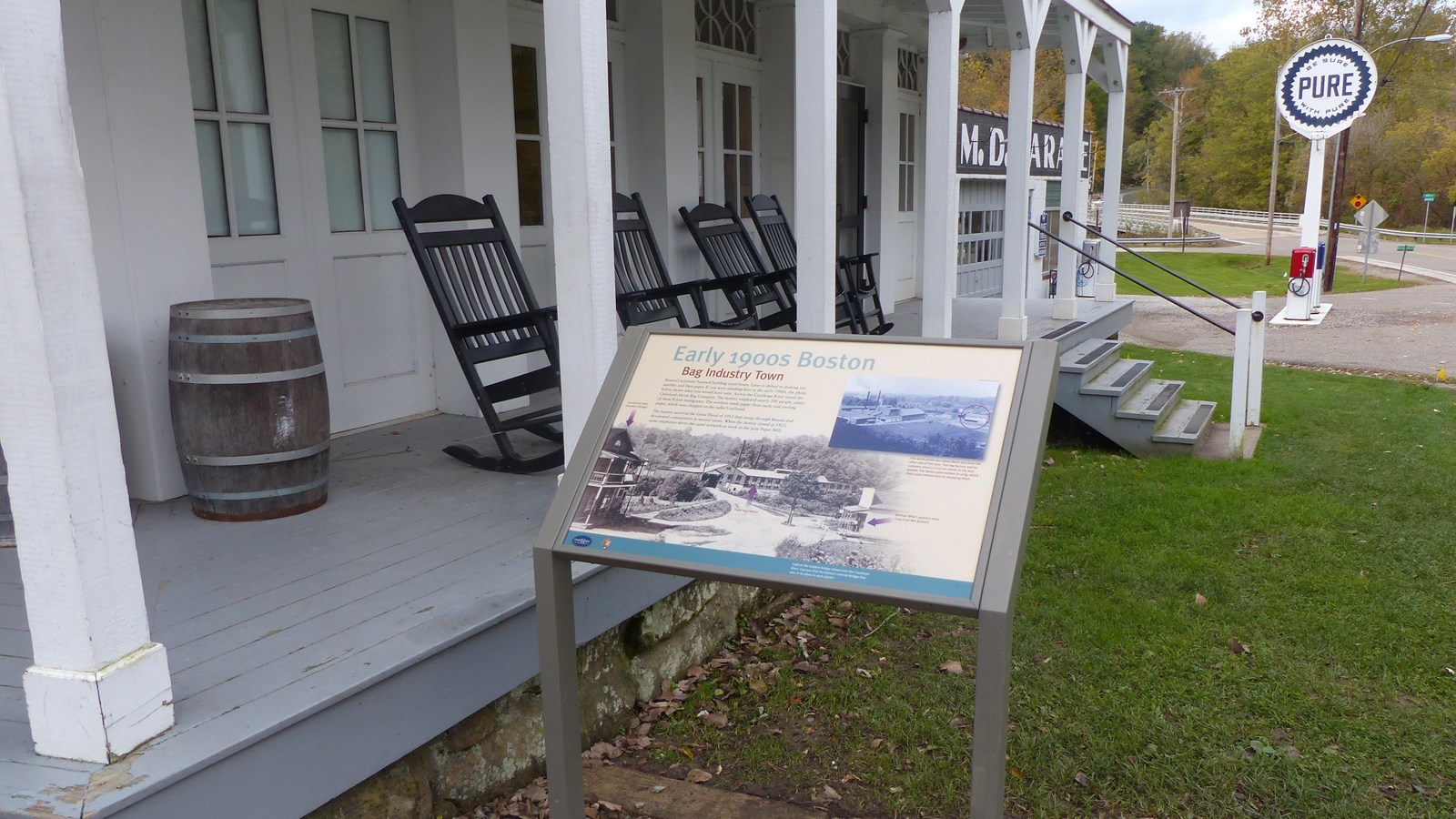 Graphic panel beside a white historic building\'s porch; rocking chairs and a barrel on the porch.