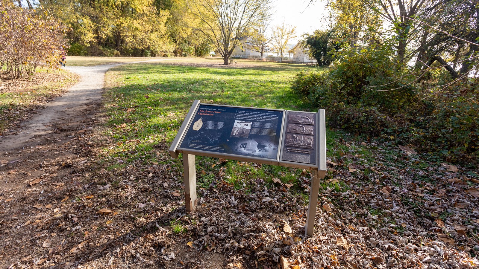 A white house and outbuilding stand near a river behind an angled wayside panel.