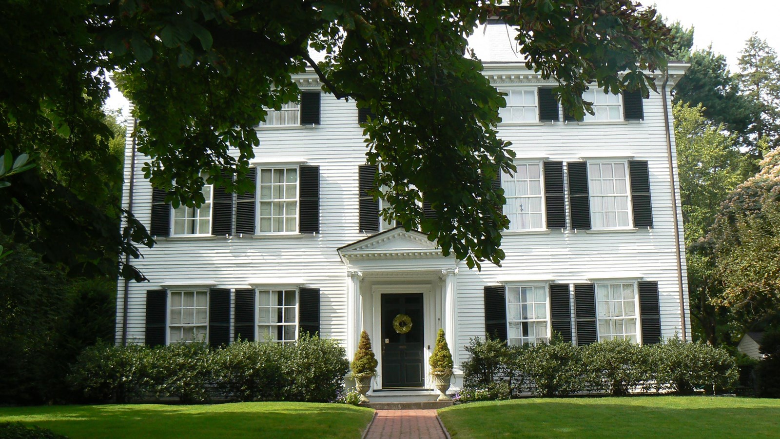 Large white three-story Georgian mansion with dark shutters and large front lawn