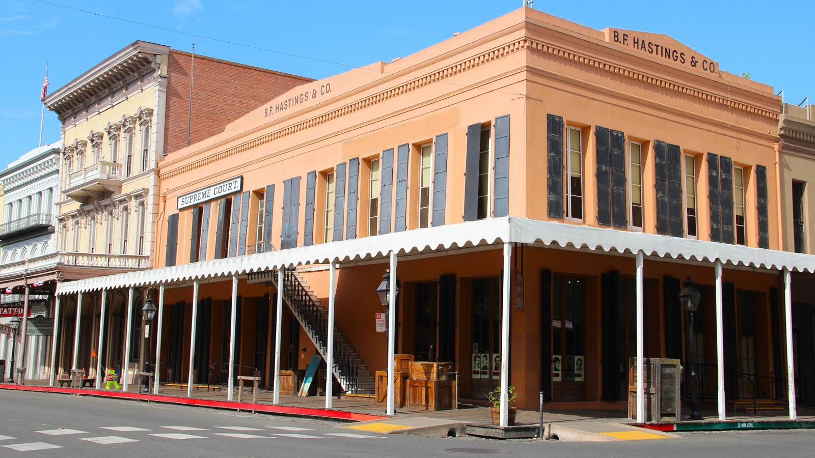 A 2-story brick building, painted orange, with a canopy over the boardwalk stands at a corner.
