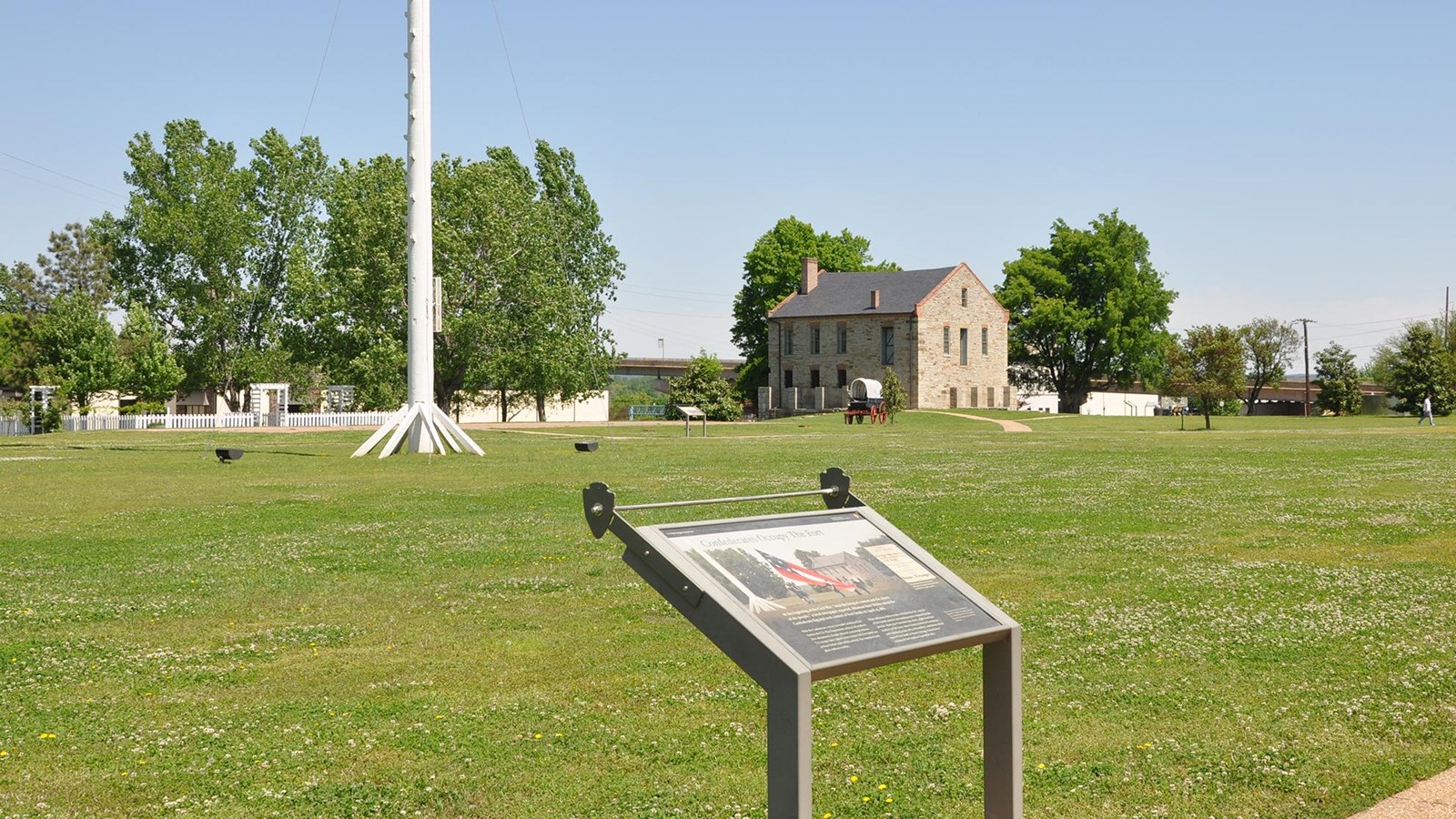 Wayside along the parade ground with the base of the flagpole and commissary in the background.