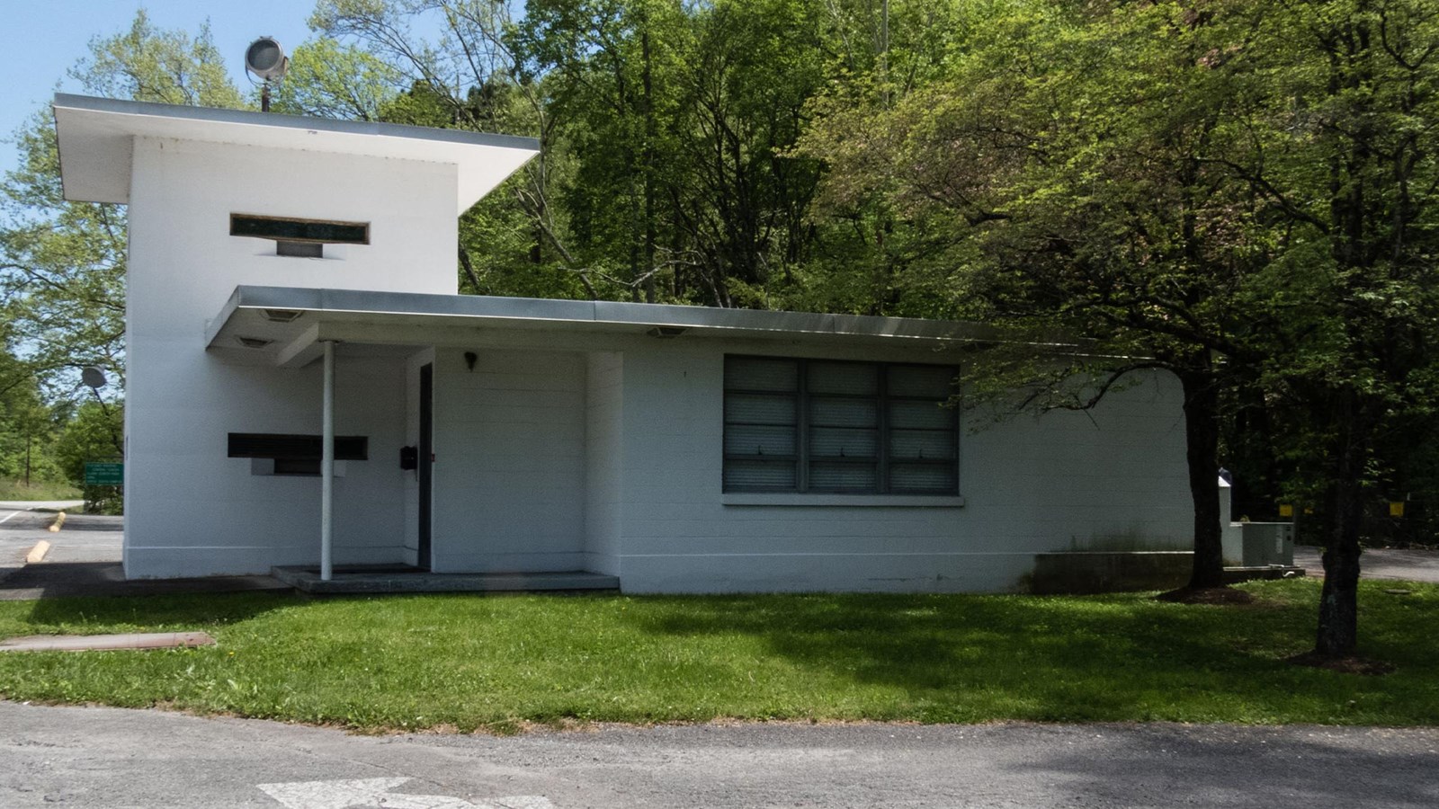 A small white concrete building with guard tower between two wooded ridges