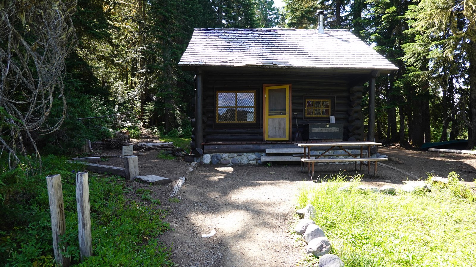 Dark brown, one story, rectangular log frame cabin with a steeply pitched cedar shake gable roof