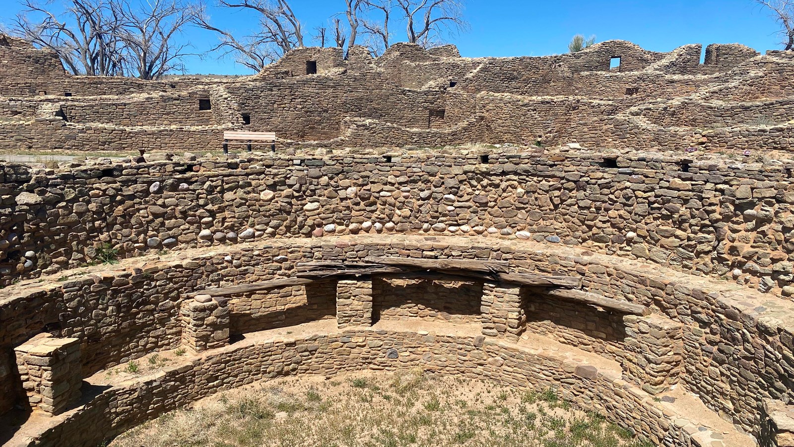 Looking down into a circular kiva with stacked stone walls and wooden remnants of a domed roof.
