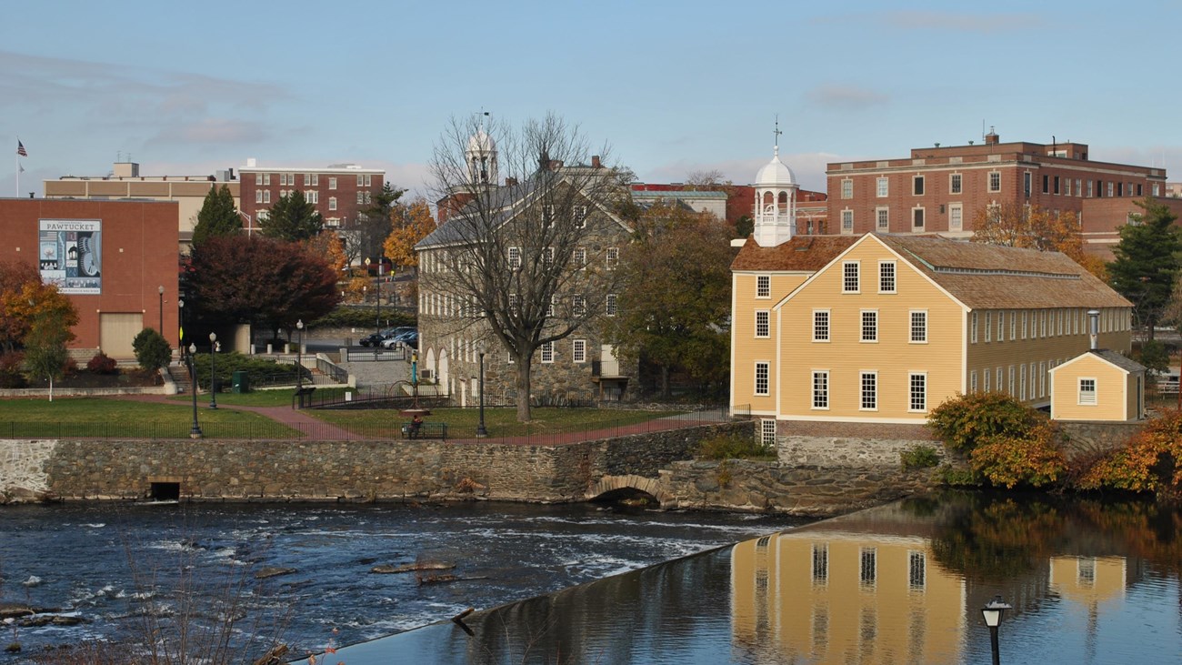 River in foreground with yellow mill and other buildings in distance