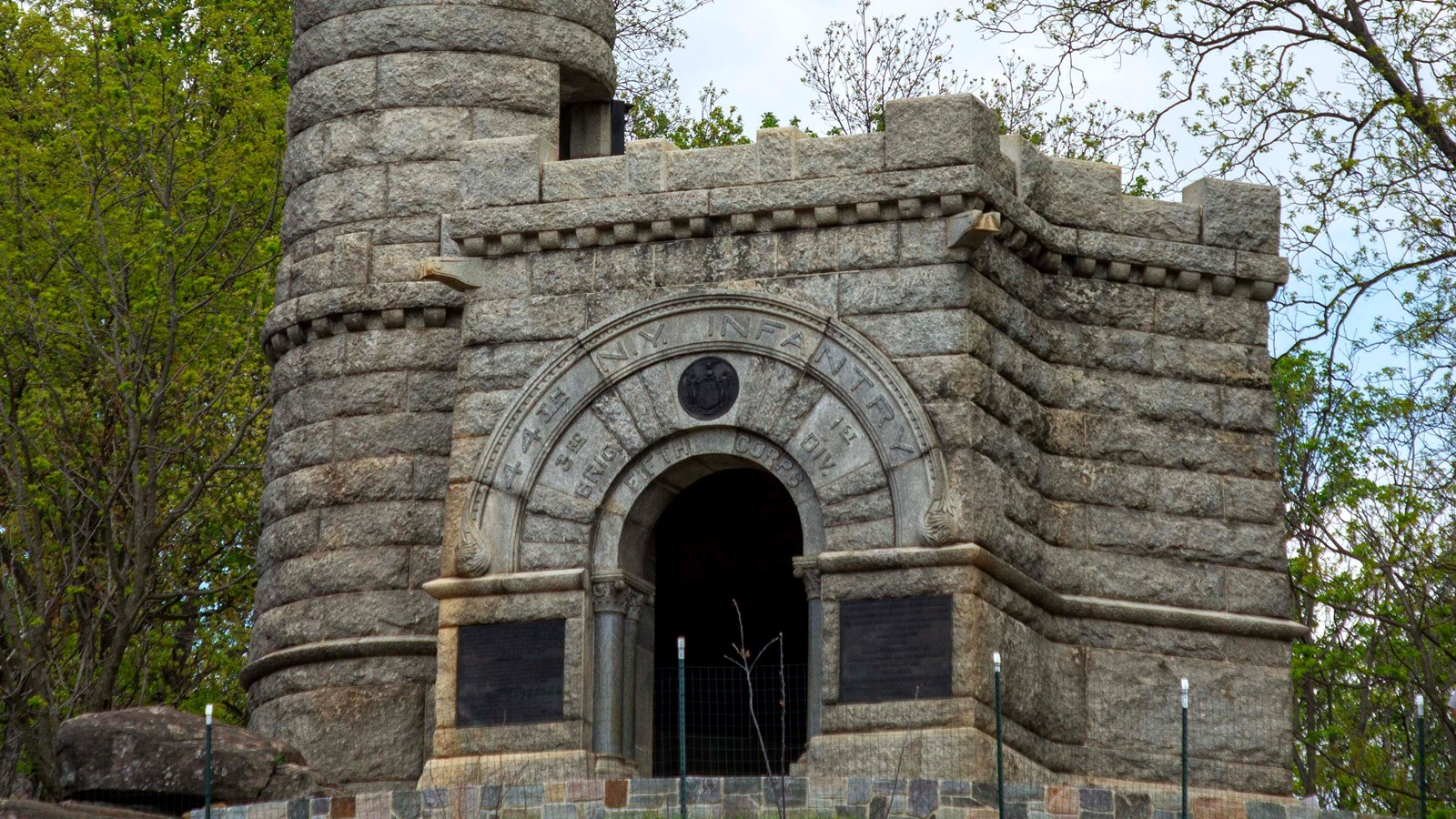 A large stone monument appears castle like near the edge of a hill near boulders.