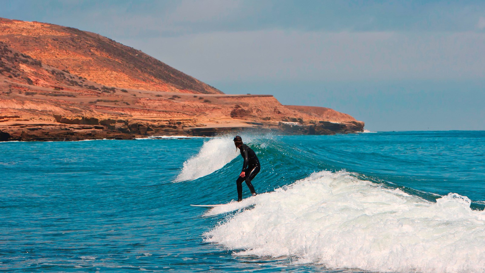 surfer in wetsuit riding wave along dry rocky shoreline